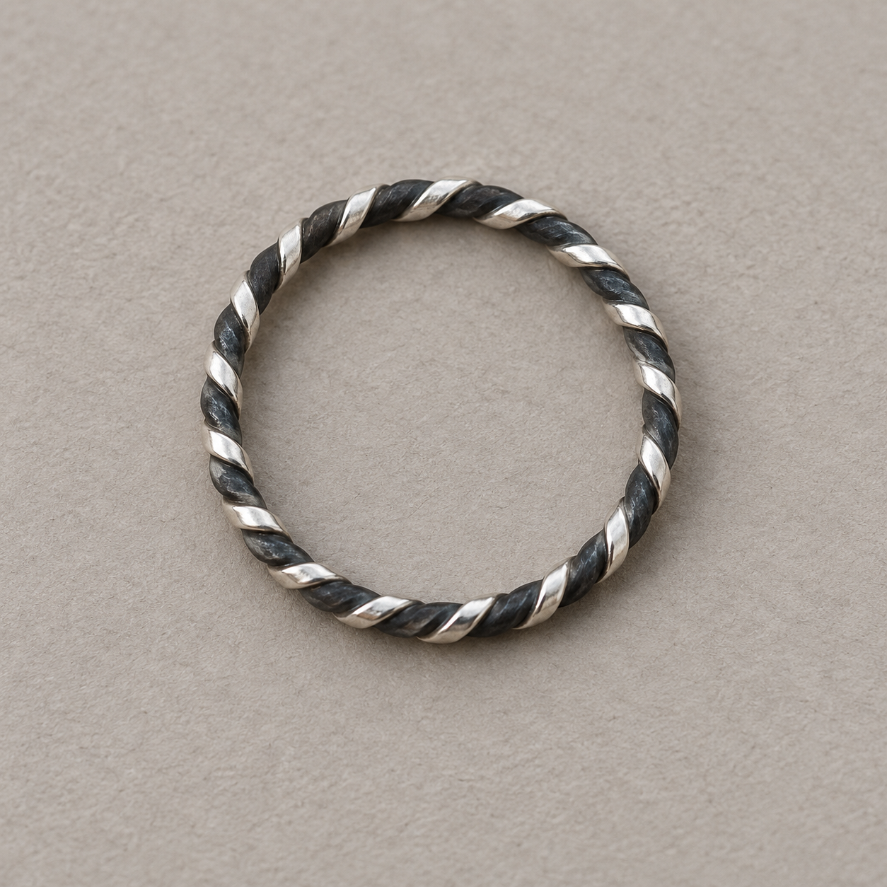 Interpretive rendering of a slender ring made from bright silver-colored and dark iron-colored twisted wires